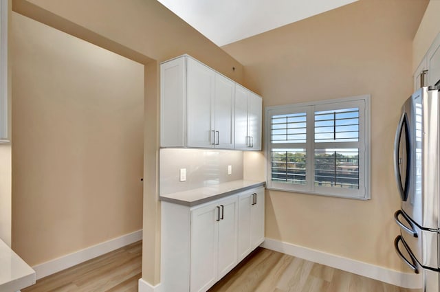 kitchen featuring light wood-type flooring, stainless steel fridge, backsplash, and white cabinetry