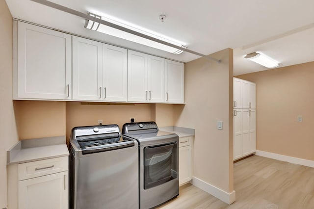 clothes washing area with cabinets, light hardwood / wood-style flooring, and washer and clothes dryer