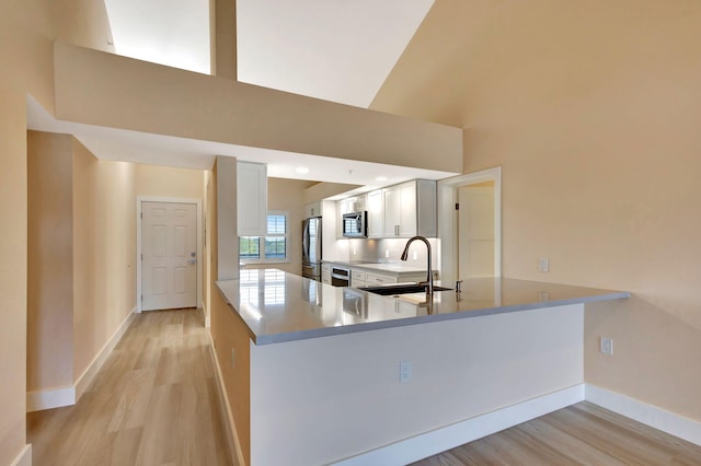 kitchen with kitchen peninsula, appliances with stainless steel finishes, sink, a high ceiling, and light hardwood / wood-style floors