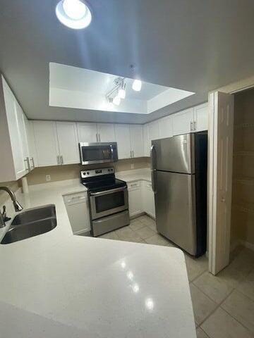 kitchen with sink, stainless steel appliances, light tile patterned floors, kitchen peninsula, and white cabinets