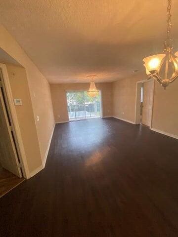 empty room with dark hardwood / wood-style flooring, a textured ceiling, and an inviting chandelier