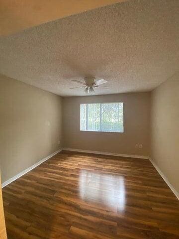 empty room with ceiling fan, dark hardwood / wood-style flooring, and a textured ceiling