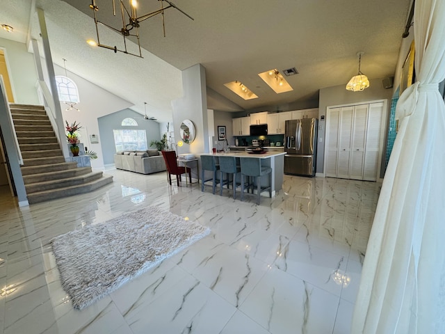 kitchen featuring white cabinetry, hanging light fixtures, stainless steel fridge with ice dispenser, high vaulted ceiling, and a breakfast bar