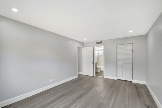 unfurnished bedroom with hardwood / wood-style flooring, connected bathroom, and a closet