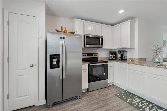 kitchen featuring white cabinets, stainless steel appliances, light hardwood / wood-style flooring, and light stone countertops