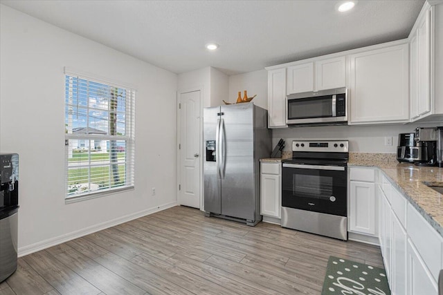 kitchen with white cabinets, stainless steel appliances, light wood-type flooring, and light stone counters