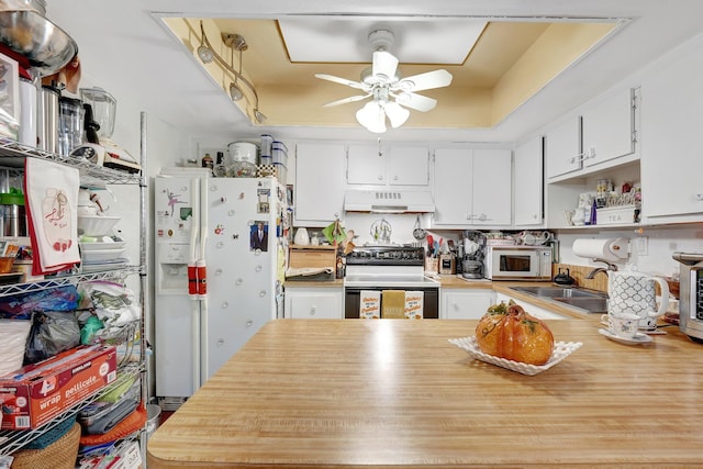 kitchen featuring white cabinetry, sink, premium range hood, white appliances, and a tray ceiling