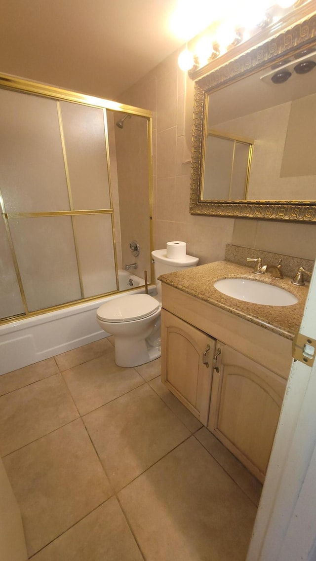 full bathroom featuring tile patterned floors, bath / shower combo with glass door, vanity, tile walls, and toilet