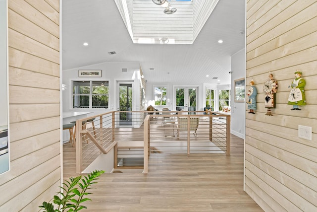 hall featuring vaulted ceiling with skylight, wood walls, and wooden ceiling