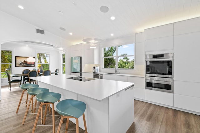 kitchen with a kitchen island, white cabinetry, stainless steel appliances, hanging light fixtures, and light hardwood / wood-style flooring