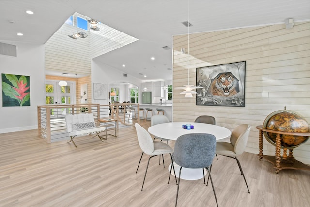 dining room featuring lofted ceiling with skylight, wooden walls, and light hardwood / wood-style flooring