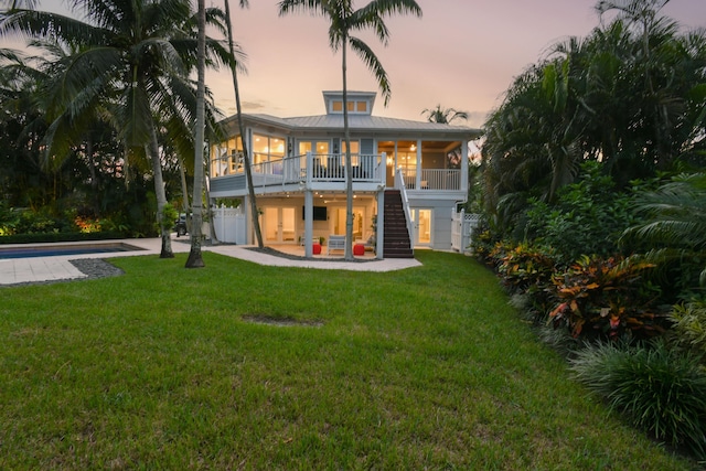 back house at dusk featuring a lawn, a patio area, and a sunroom