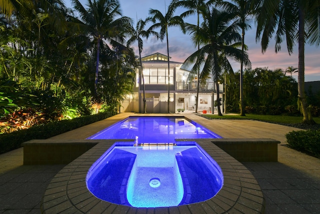 pool at dusk with an in ground hot tub and a patio area