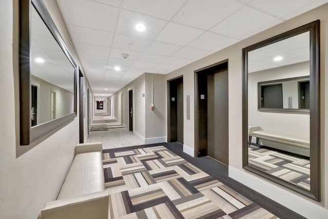 hallway with a paneled ceiling, elevator, and light colored carpet