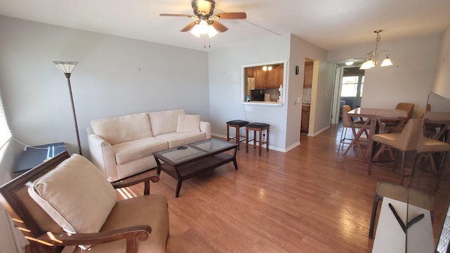 living room with ceiling fan with notable chandelier and light hardwood / wood-style flooring