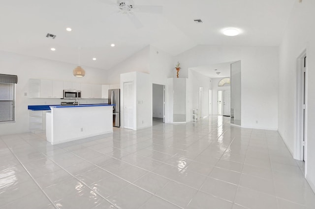 kitchen with stainless steel appliances, light tile patterned floors, high vaulted ceiling, white cabinets, and a center island