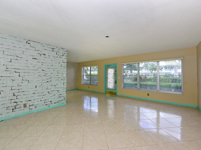 tiled spare room with brick wall, a healthy amount of sunlight, and a textured ceiling