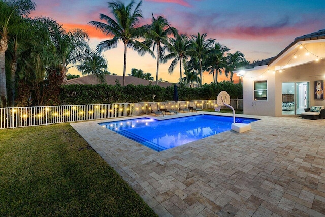 pool at dusk with a lawn and a patio area