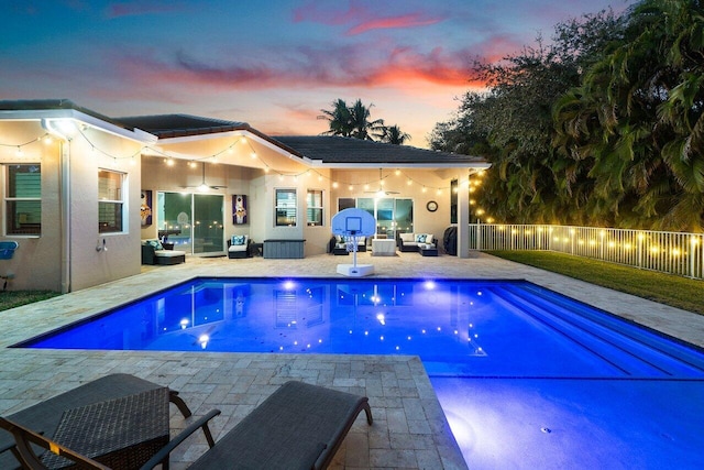 pool at dusk with outdoor lounge area, ceiling fan, and a patio area