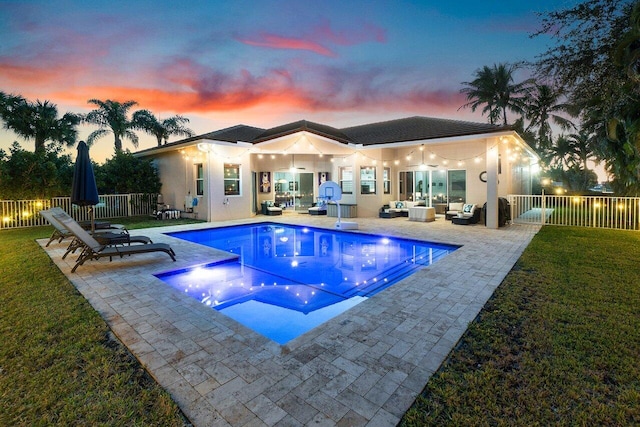 pool at dusk featuring an outdoor living space, a patio area, and a lawn