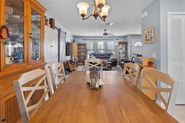 dining room with a barn door, ceiling fan with notable chandelier, and a textured ceiling