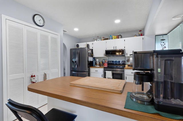 kitchen featuring white cabinetry, appliances with stainless steel finishes, kitchen peninsula, and decorative backsplash