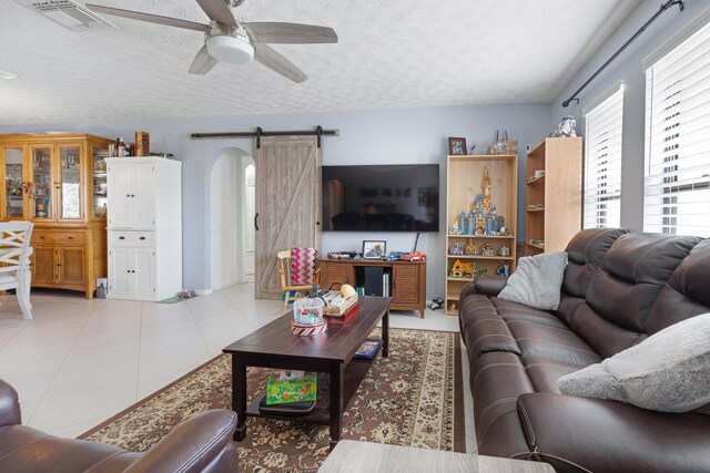 tiled living room with ceiling fan, a barn door, and a textured ceiling