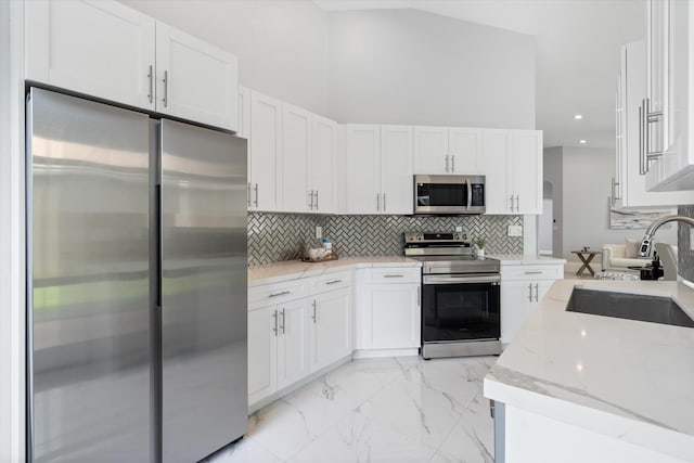 kitchen featuring sink, light stone countertops, a towering ceiling, white cabinetry, and stainless steel appliances