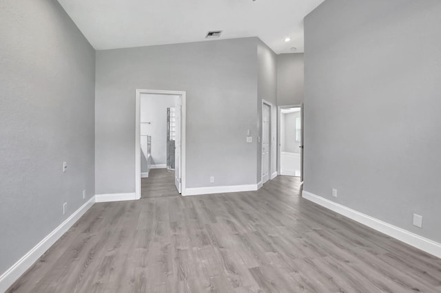 unfurnished living room featuring light wood-type flooring and a towering ceiling