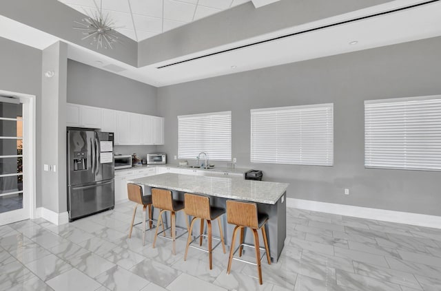 kitchen with a center island, appliances with stainless steel finishes, light stone counters, white cabinetry, and a breakfast bar area