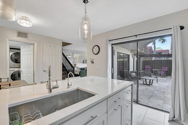 kitchen featuring sink, hanging light fixtures, light tile patterned floors, white cabinetry, and stacked washer / dryer