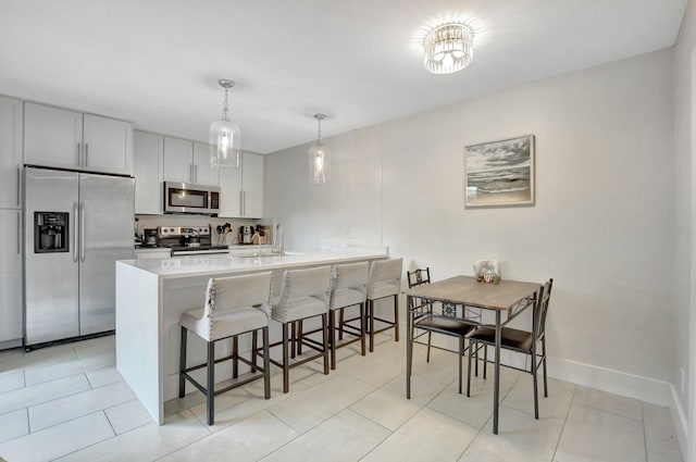 kitchen featuring stainless steel appliances, kitchen peninsula, pendant lighting, a kitchen bar, and white cabinets