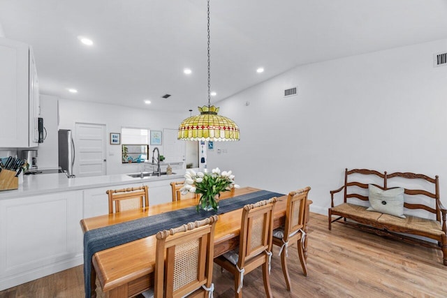 dining space with vaulted ceiling, sink, and light hardwood / wood-style flooring