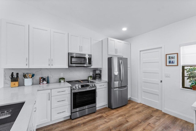 kitchen with appliances with stainless steel finishes, tasteful backsplash, sink, hardwood / wood-style flooring, and white cabinetry