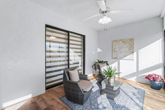 living area featuring ceiling fan, wood-type flooring, and a textured ceiling