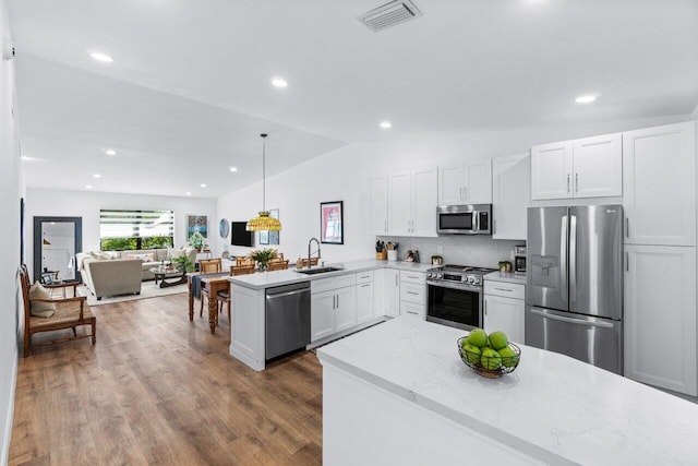 kitchen featuring kitchen peninsula, appliances with stainless steel finishes, sink, white cabinets, and hanging light fixtures