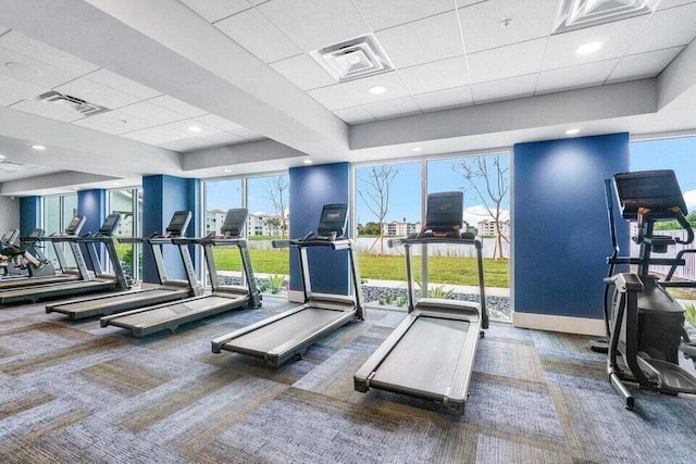 workout area with expansive windows, dark carpet, a wealth of natural light, and a tray ceiling