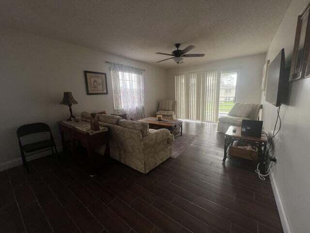 living room featuring ceiling fan, a textured ceiling, and dark wood-type flooring