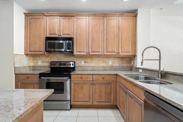 kitchen featuring appliances with stainless steel finishes, light tile patterned floors, light stone counters, and sink