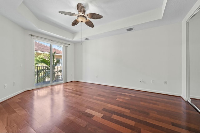 spare room with a tray ceiling, ceiling fan, and dark hardwood / wood-style floors