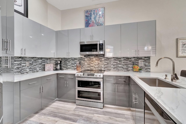 kitchen with gray cabinetry, light stone countertops, sink, backsplash, and appliances with stainless steel finishes