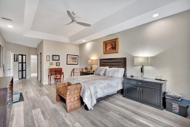 bedroom with a raised ceiling, ceiling fan, and light wood-type flooring