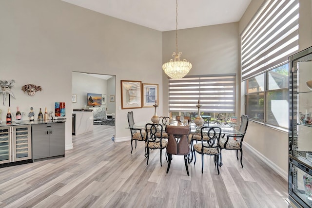 dining space with wine cooler, light hardwood / wood-style flooring, a towering ceiling, and a notable chandelier