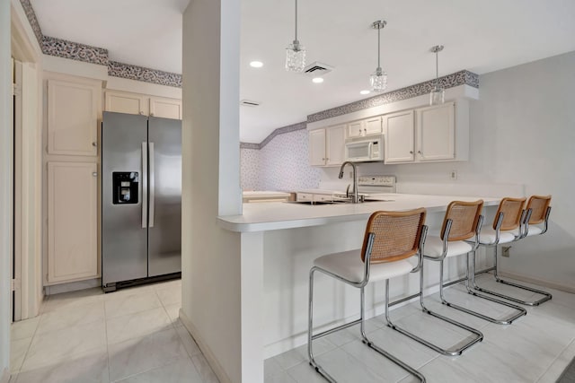 kitchen with a kitchen bar, hanging light fixtures, sink, kitchen peninsula, and stainless steel fridge