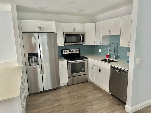 kitchen with appliances with stainless steel finishes, white cabinetry, sink, decorative backsplash, and light hardwood / wood-style floors