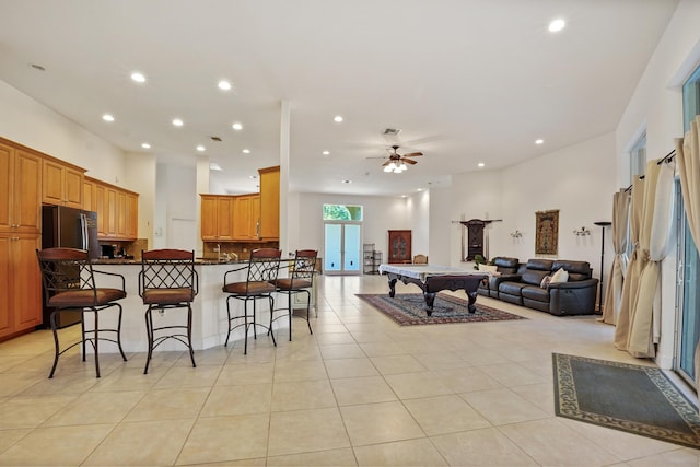 kitchen featuring stainless steel refrigerator, kitchen peninsula, a breakfast bar area, light tile patterned flooring, and pool table