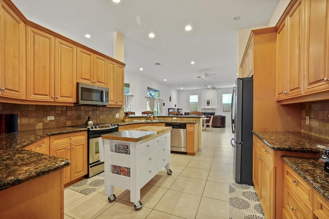 kitchen featuring kitchen peninsula, appliances with stainless steel finishes, ceiling fan, dark stone countertops, and a center island