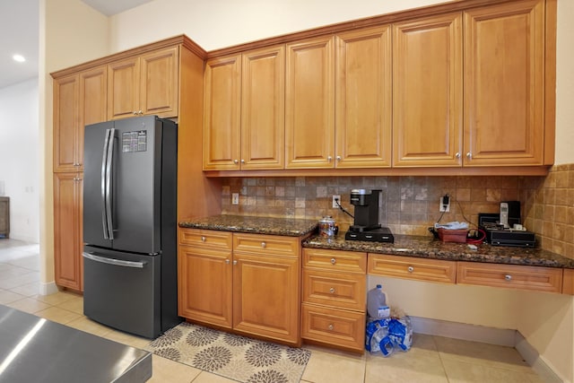 kitchen featuring decorative backsplash, light tile patterned flooring, dark stone countertops, and stainless steel refrigerator