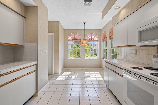 kitchen with white appliances, backsplash, light tile patterned floors, decorative light fixtures, and white cabinetry