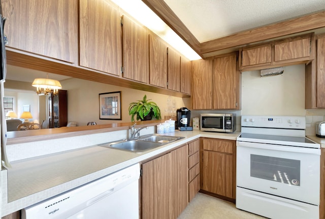 kitchen featuring kitchen peninsula, white appliances, an inviting chandelier, and sink